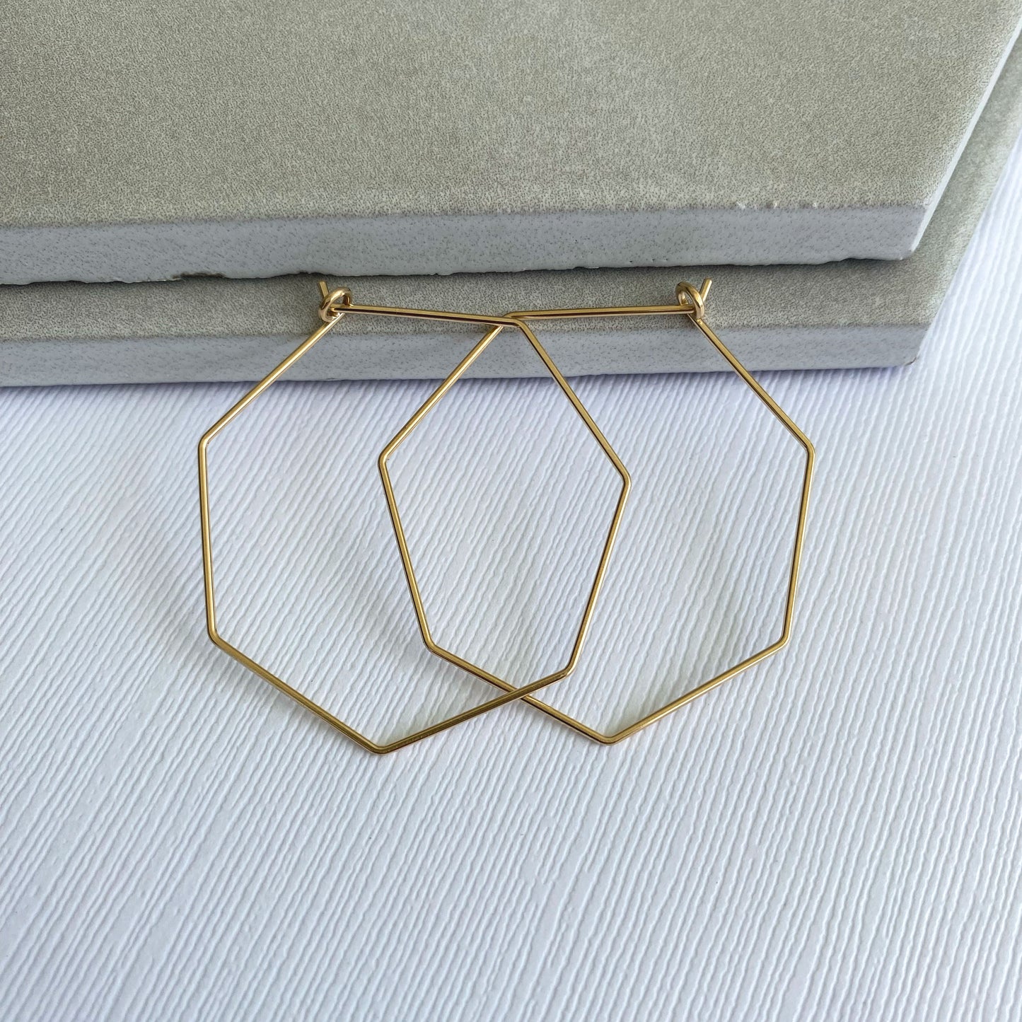 Flat lay of 14k gold-filled heptagon hoop earrings, emphasizing their unique seven-sided shape.