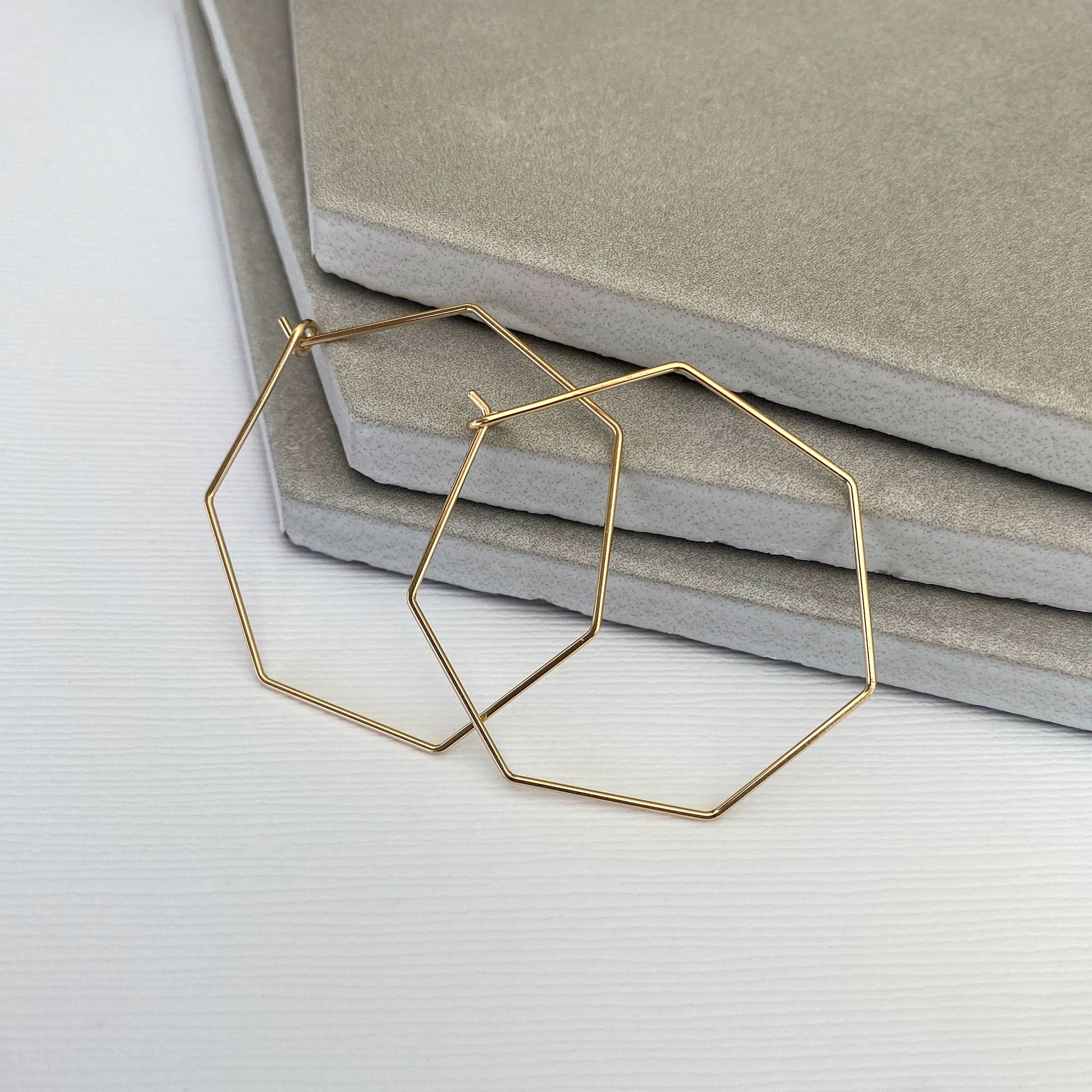 Close-up of 14k gold-filled heptagon hoop earrings showing the seven-sided geometric design.