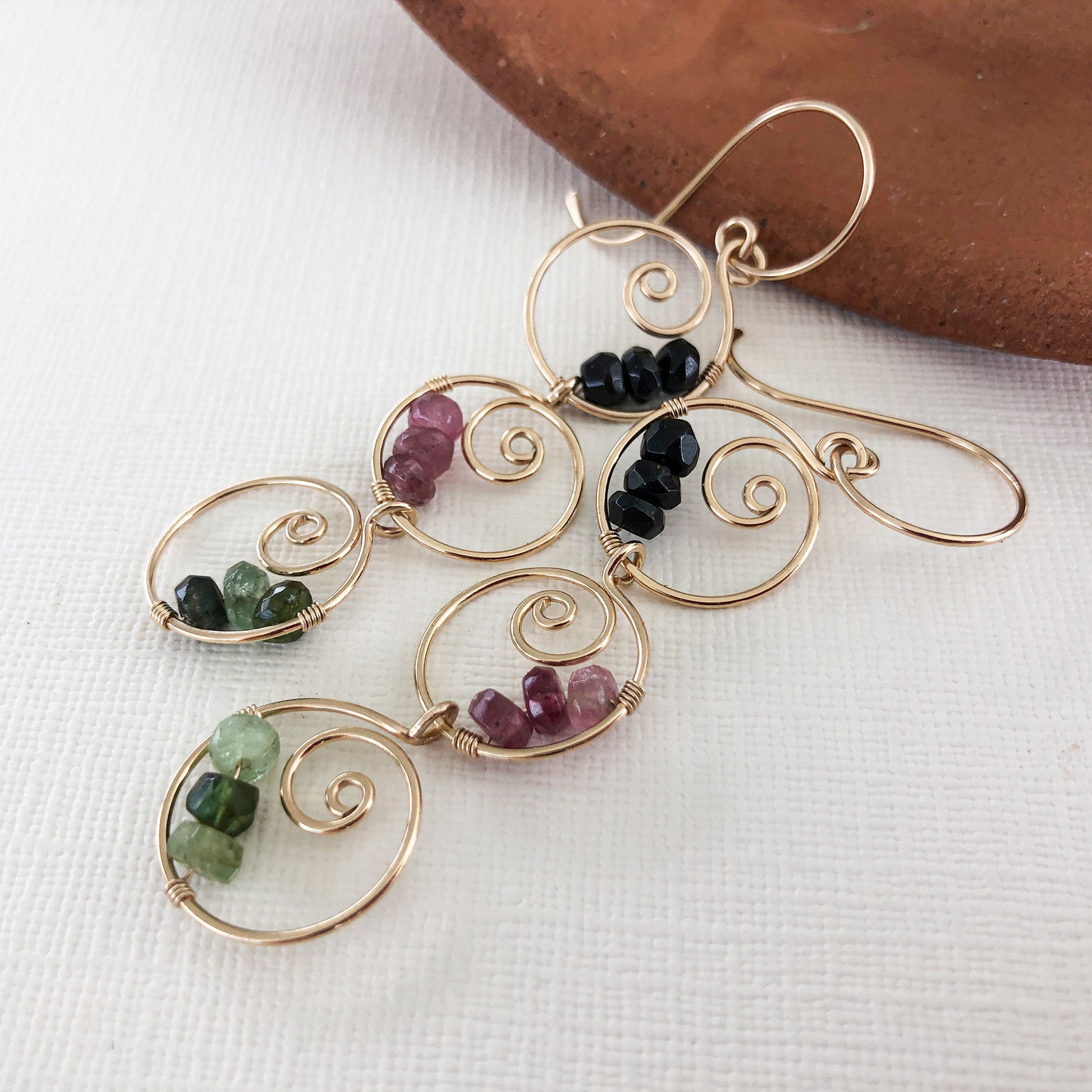 Close-up of gemstone details – A zoomed-in image of the black, green, and pink tourmaline stones wire-wrapped onto the gold-filled spiral hoops.