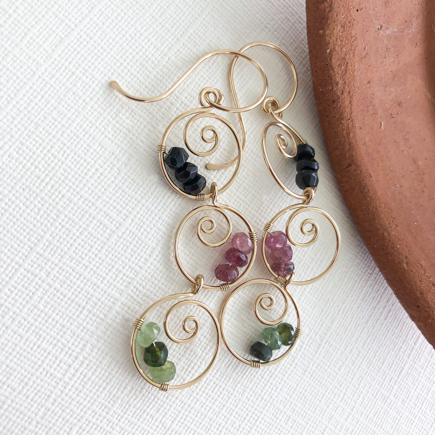 Close-up of gemstone details – A zoomed-in image of the black, green, and pink tourmaline stones wire-wrapped onto the gold-filled spiral hoops.