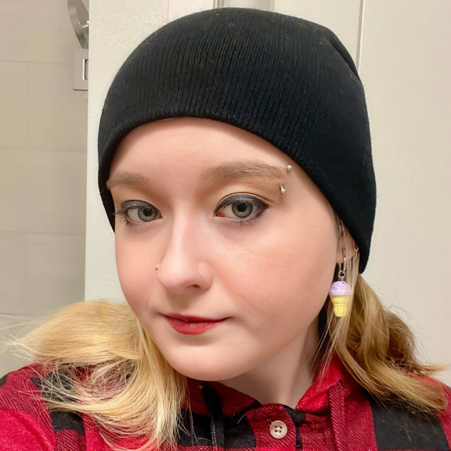 Person wearing a black beanie and red plaid shirt with a neutral background