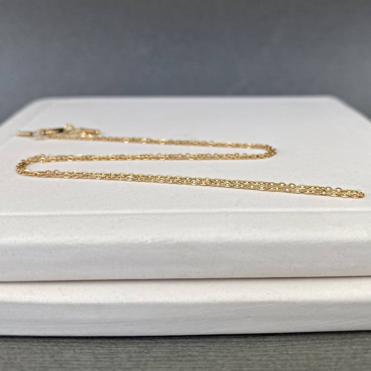 A close-up of a dainty 14k gold filled chain laid next to a ruler, showing the exact 0.9mm width of the links.