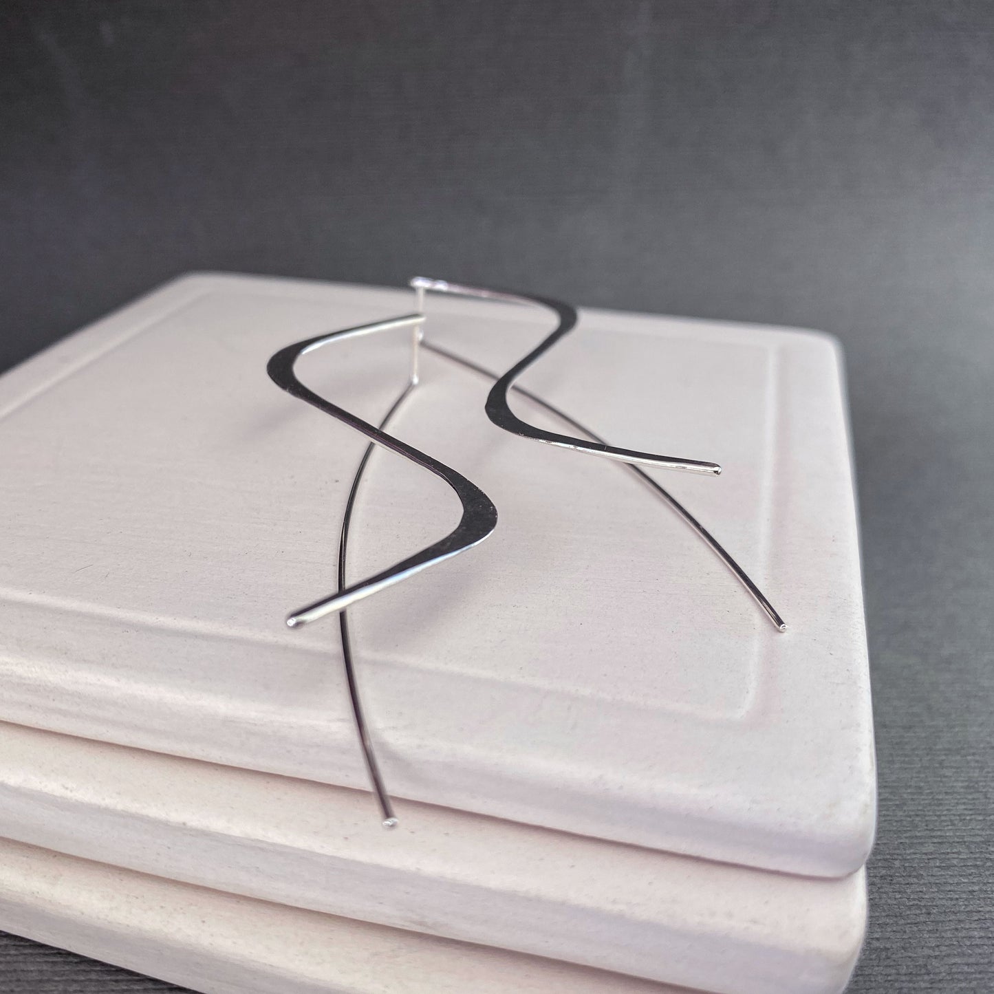 A flat lay photo of the lightweight sterling silver earrings on a textured background, emphasizing their modern design.