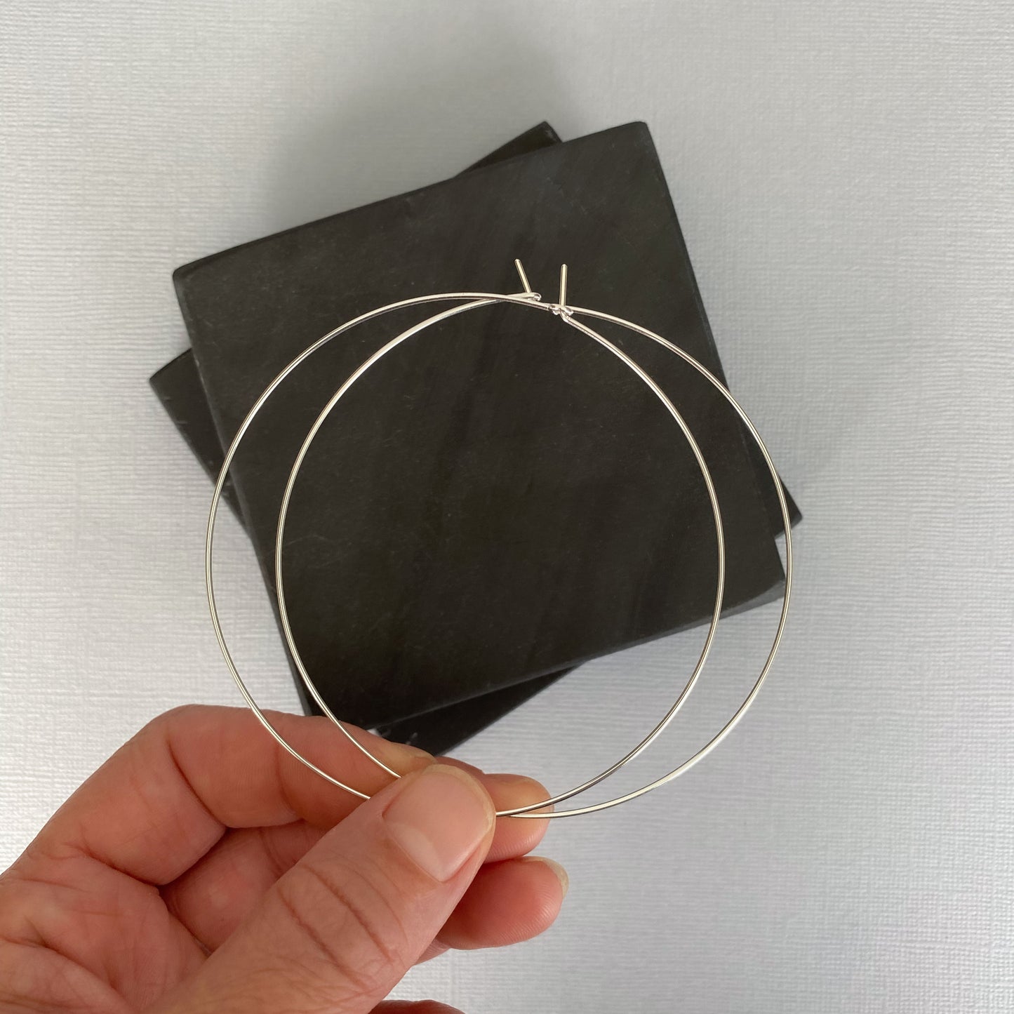 A hand holding sterling silver hoop earrings, displaying their smooth finish and quality craftsmanship.