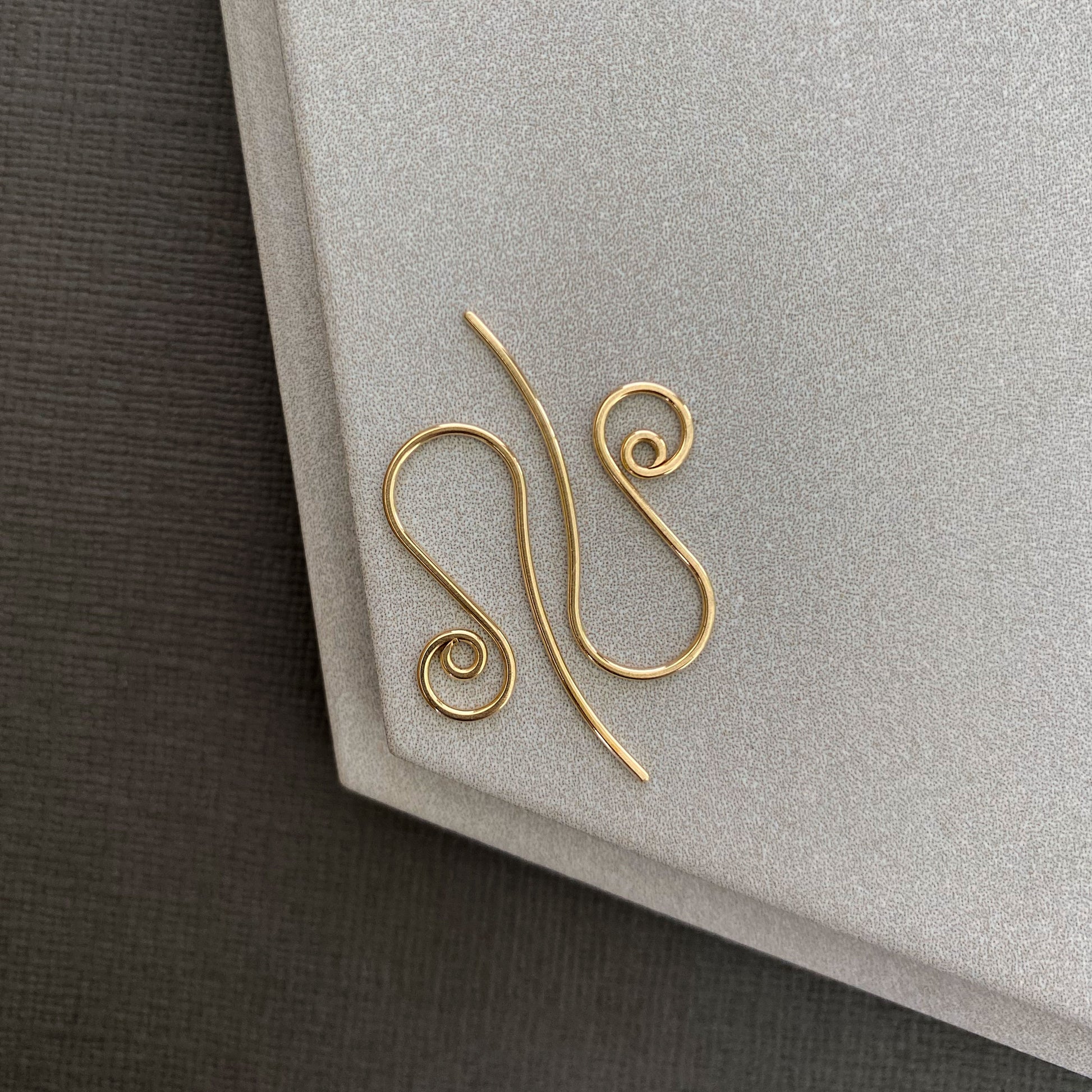 10K gold spiral earring hooks displayed on a hand, highlighting their delicate size and design.