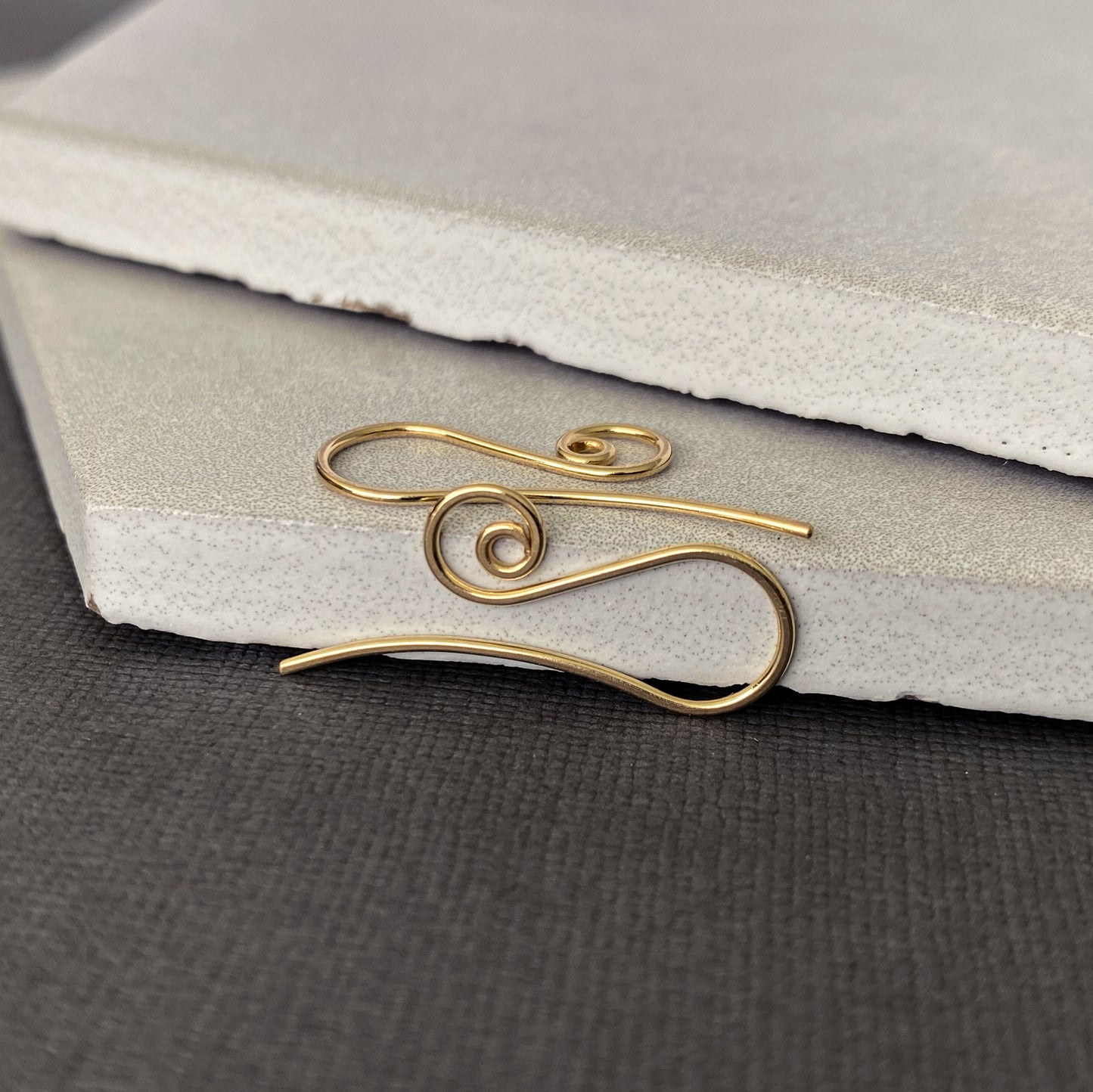 Detailed close-up of spiral-shaped 10K solid gold earring hooks, crafted for comfort and durability.