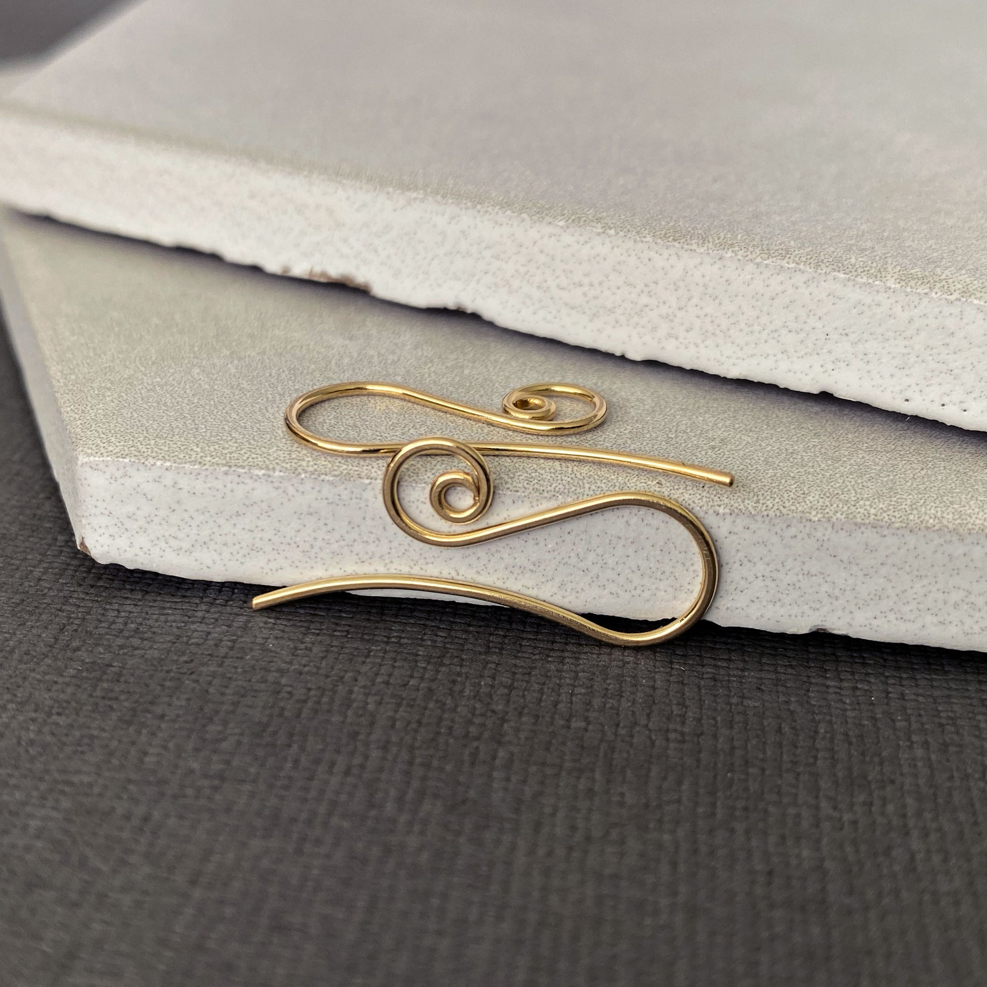 Detailed close-up of spiral-shaped 10K solid gold earring hooks, crafted for comfort and durability.