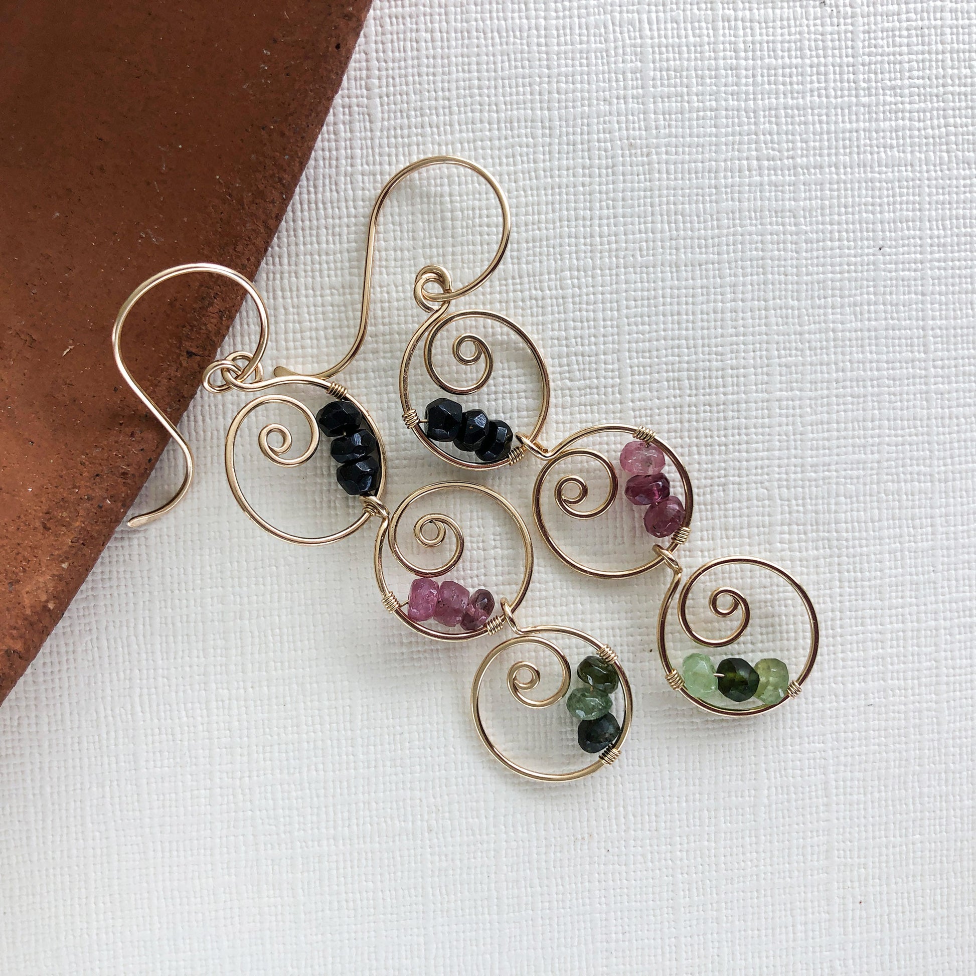 Close-up of multicolor tourmaline dangle earrings – Handmade earrings featuring six gold-filled spiral hoops with wire-wrapped black, green, and pink tourmaline gemstones.