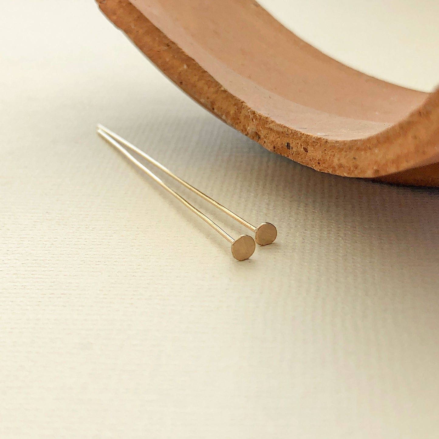 A pair of 2"Gold filled head pins next to a broken clay planter organic round shape hand hammered