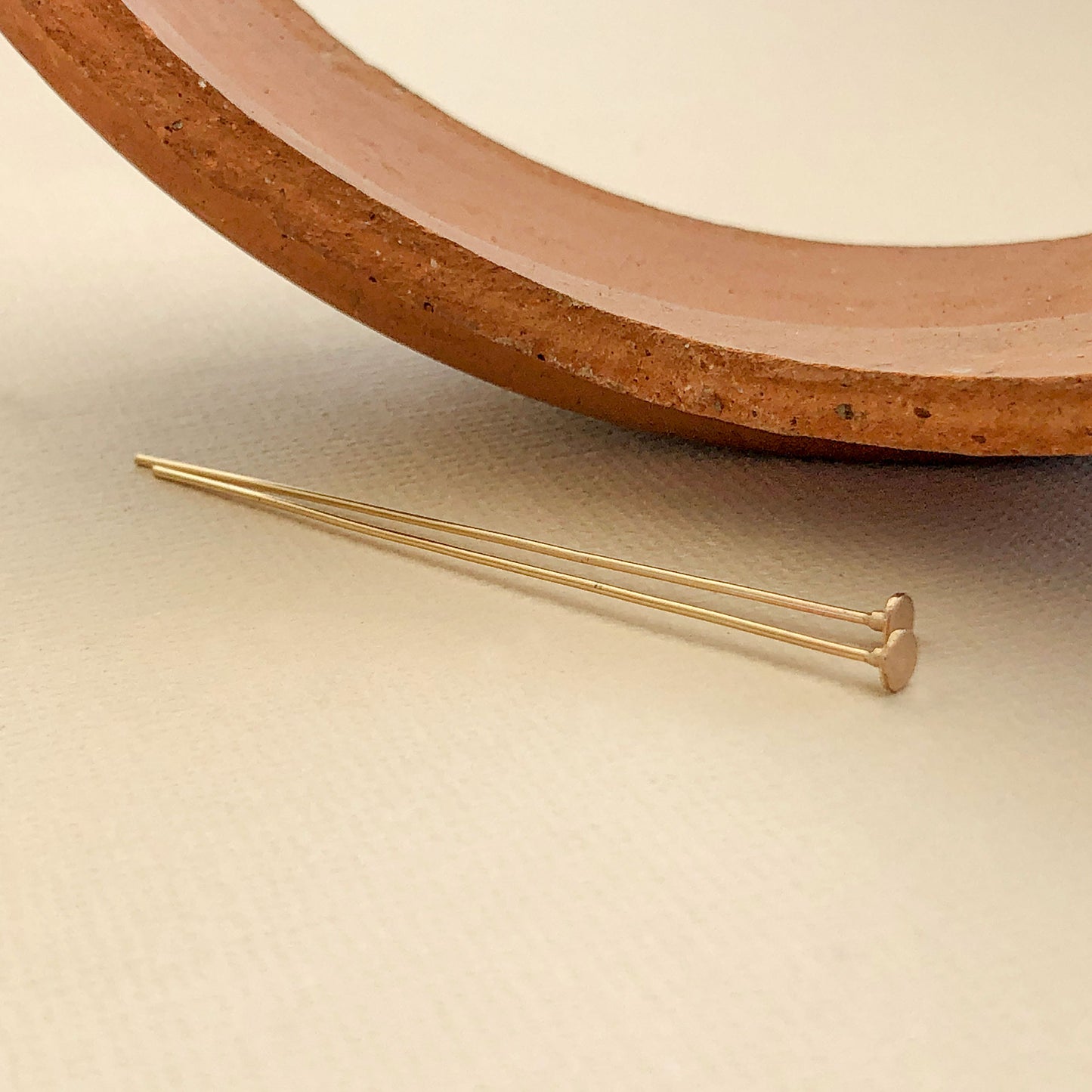 A pair of gold filled head pins that measure 2" these are handmade and are pictured next to a broken clay pot. The ends feature 14k gold.