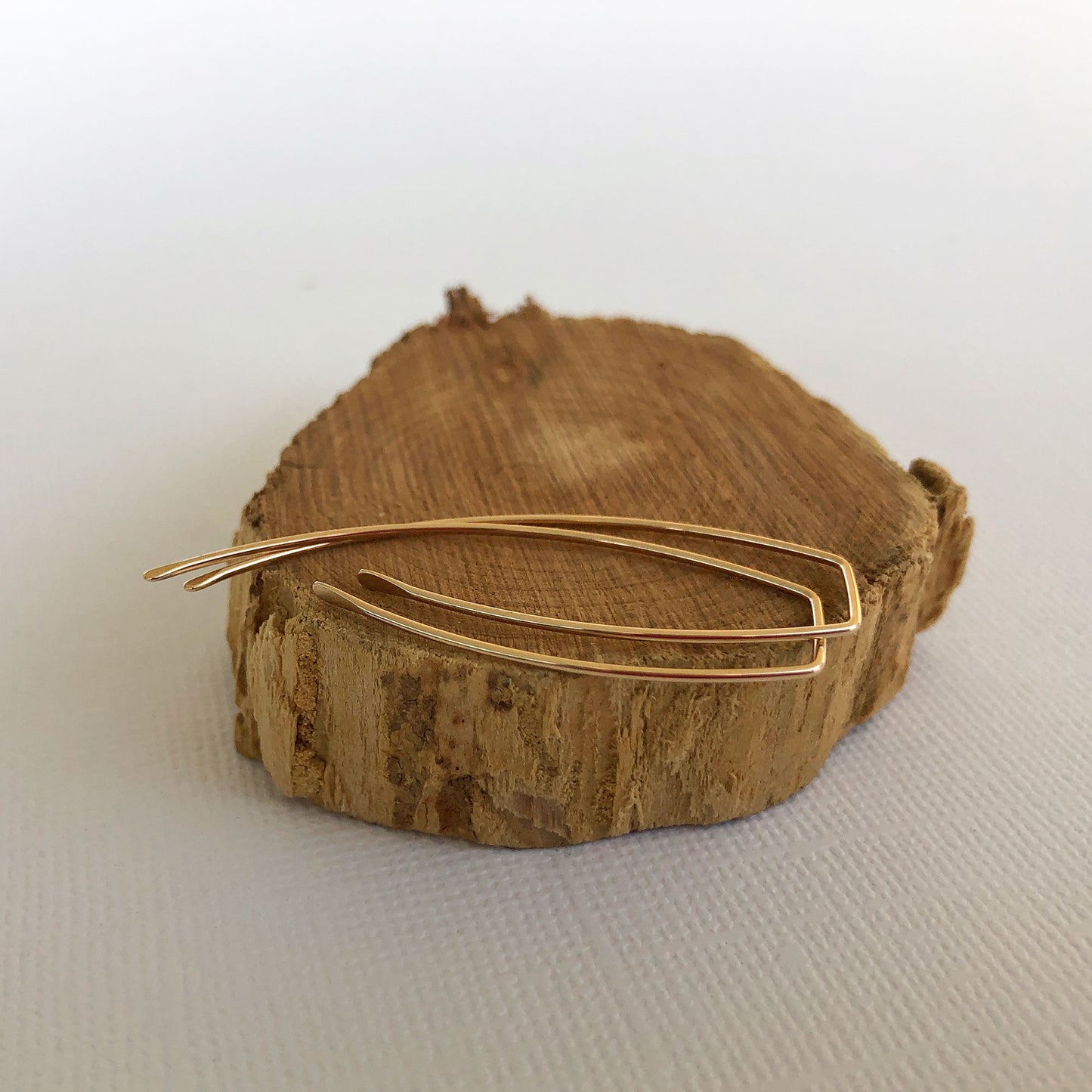 gold filled threader earrings laying on a wooden block. You can wear them as is or wrap beads around them.