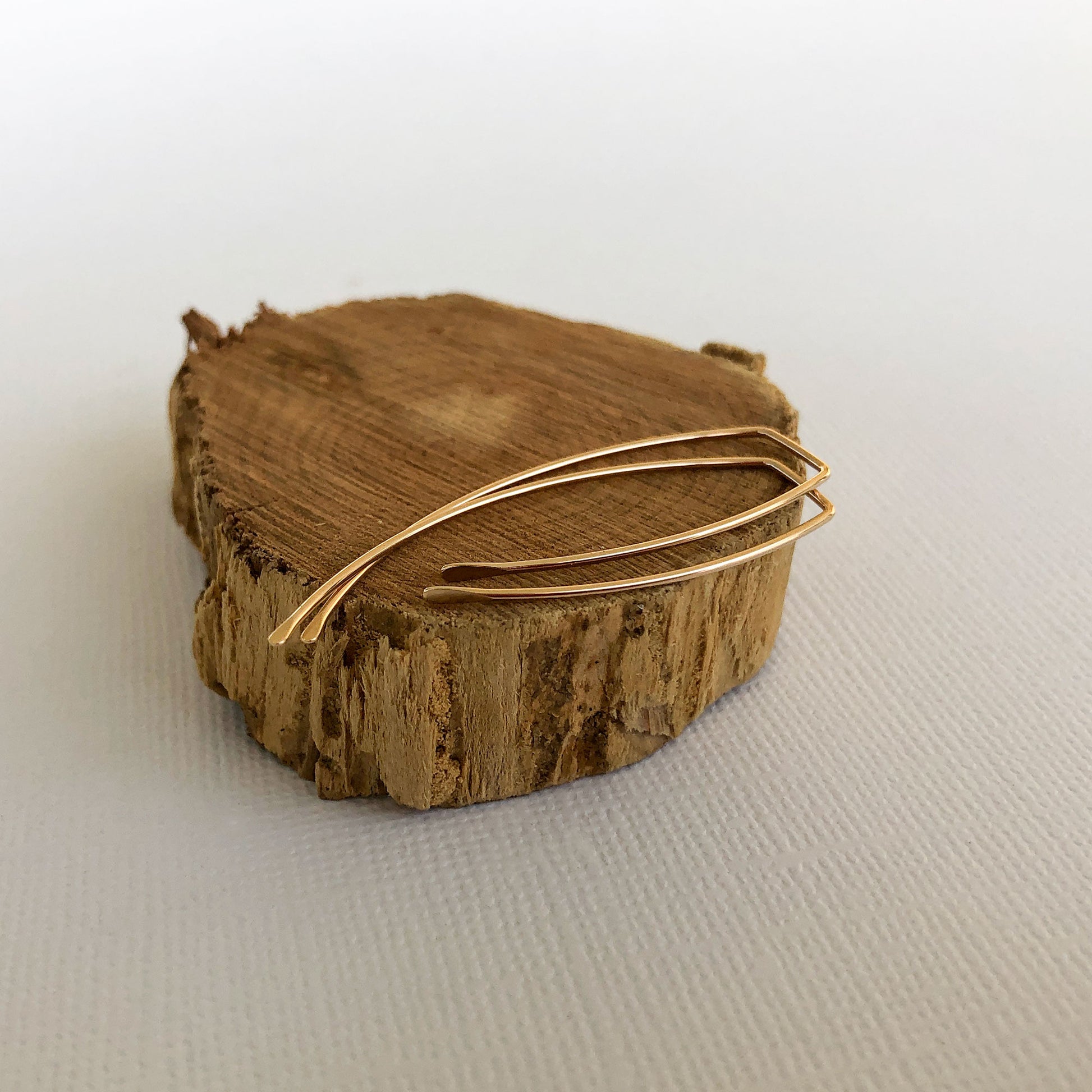 gold filled ear wire handmade are laying on their side on a wooden block.  They have been hammered in the front and the back.