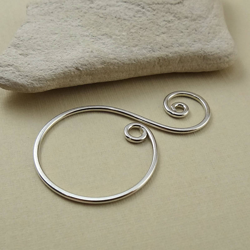 Side angle of a sterling silver spiral drop charm, showing its smooth curves and hammered texture.