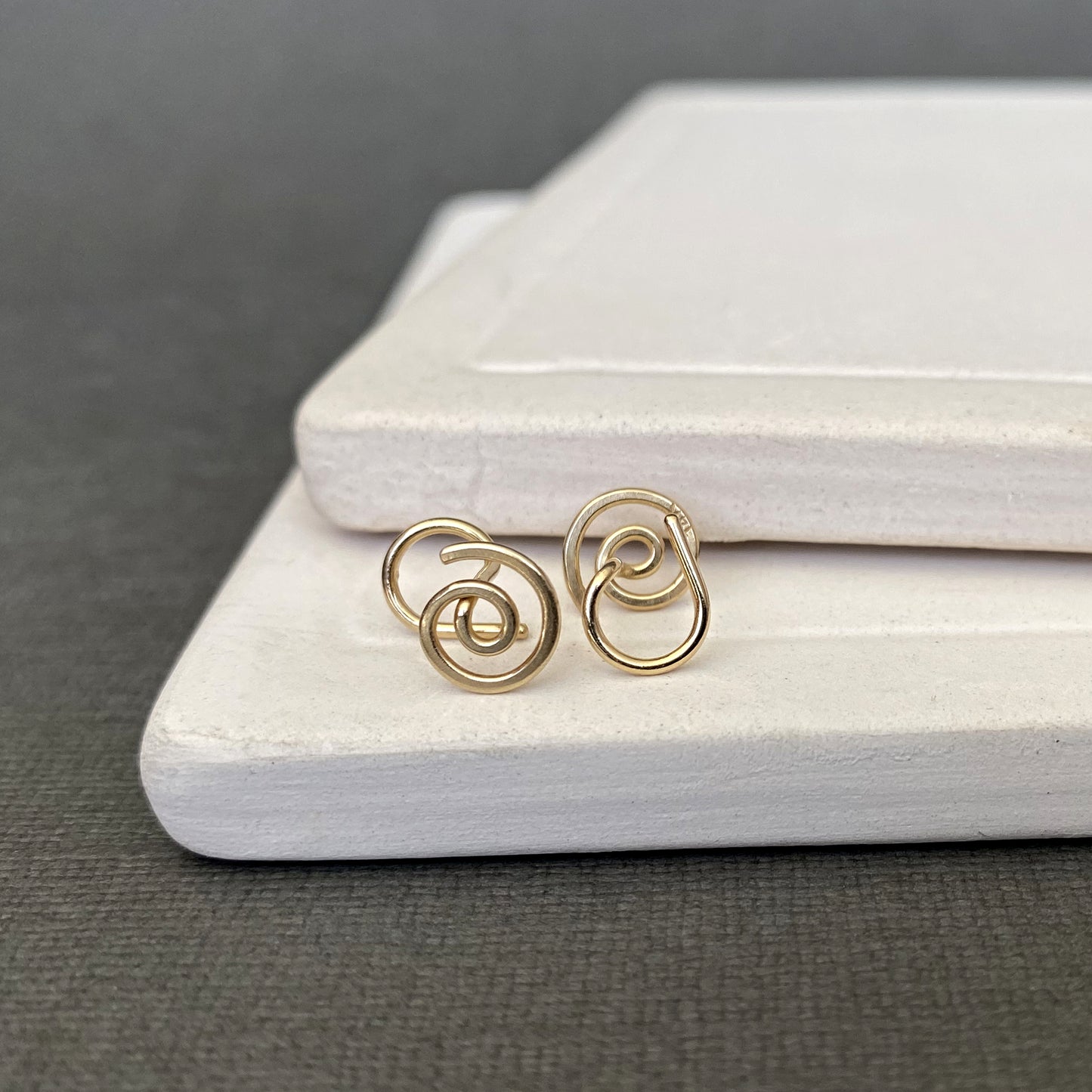 Gold spiral earrings on a white jewelry box with a gray background