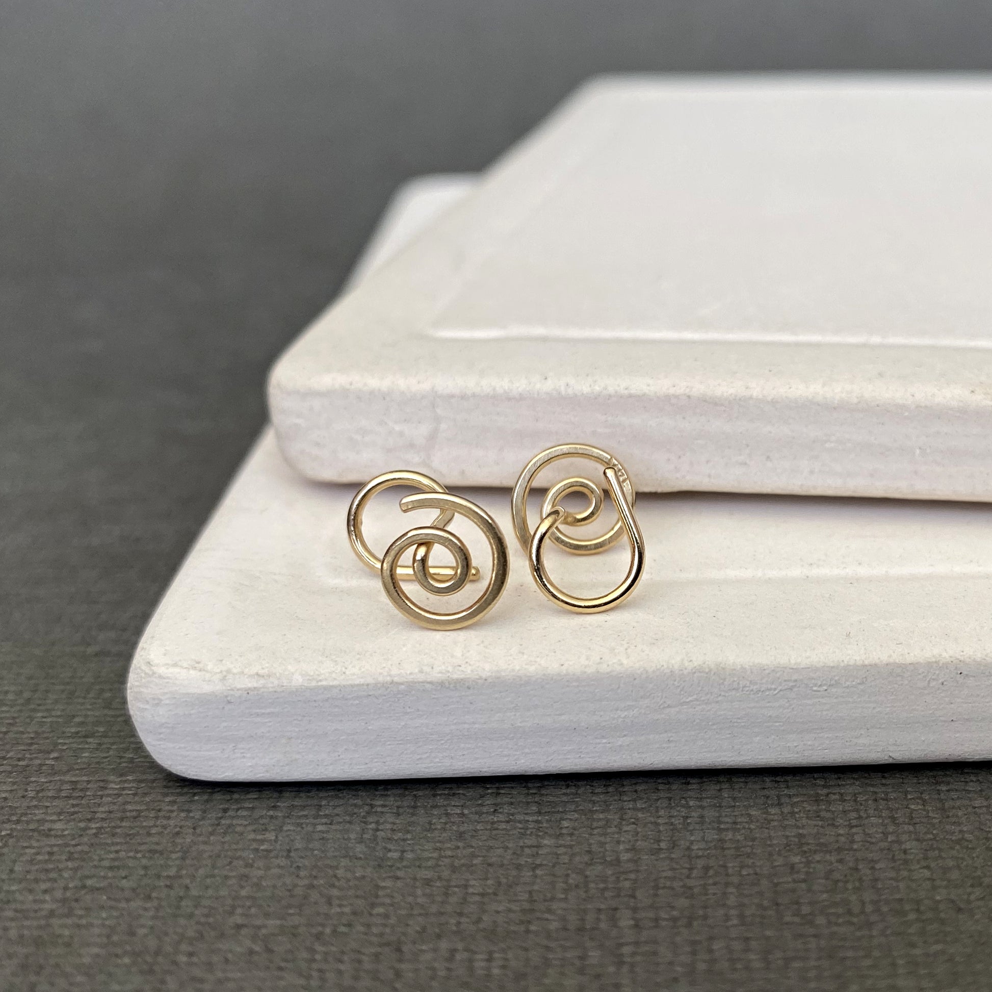 Gold spiral earrings on a white jewelry box with a gray background