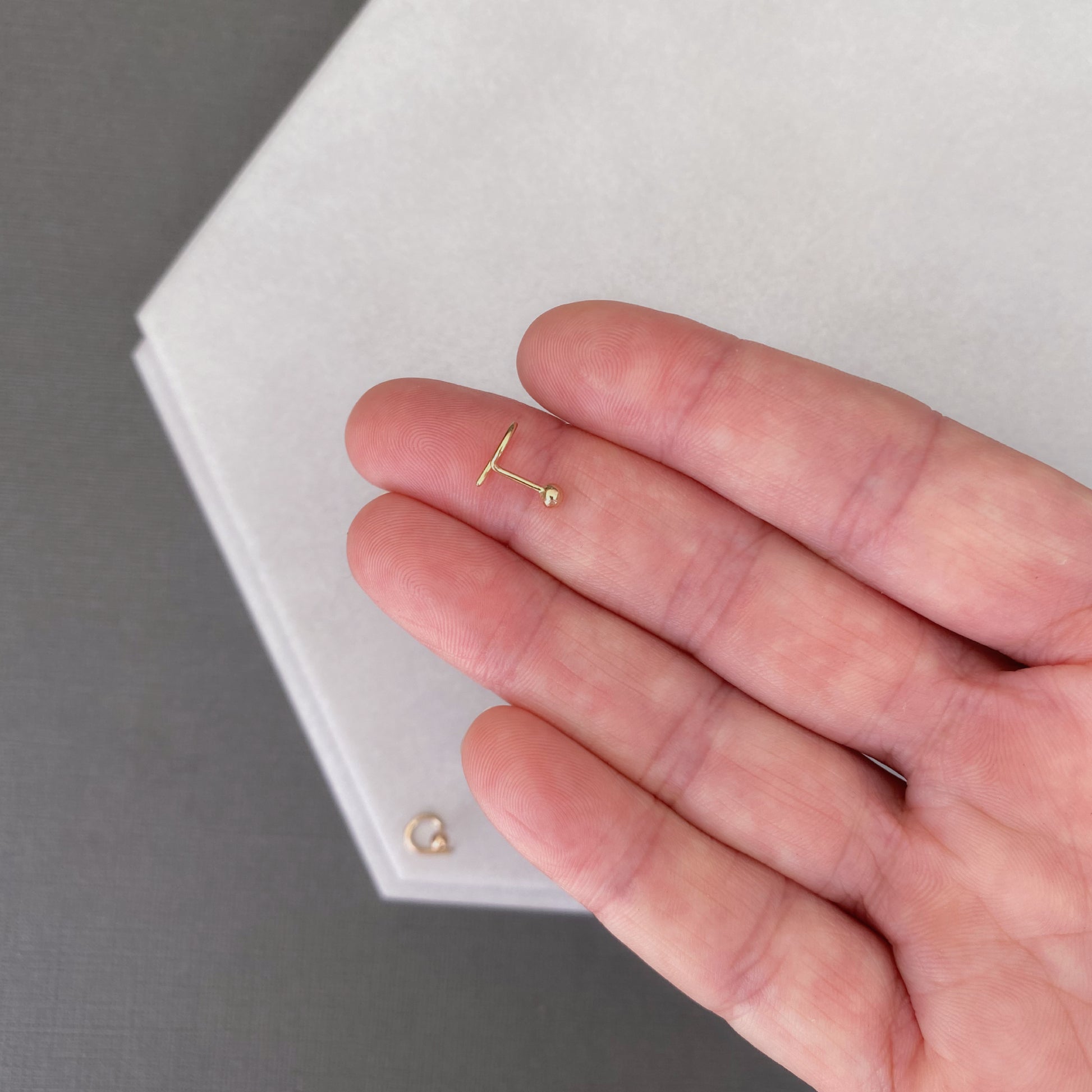 Gold earring on a hand with a white box in the background