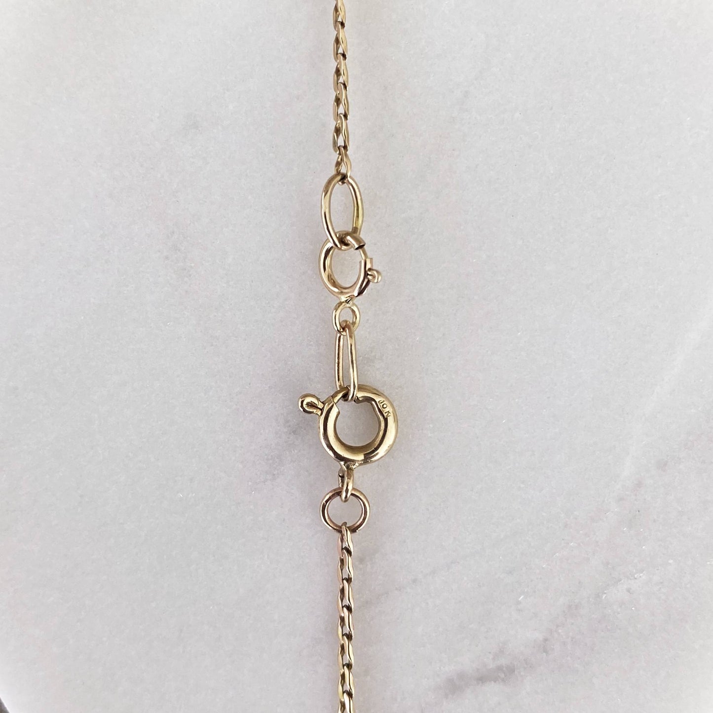 14k gold charm holder clipped onto dainty gold chain on marble display