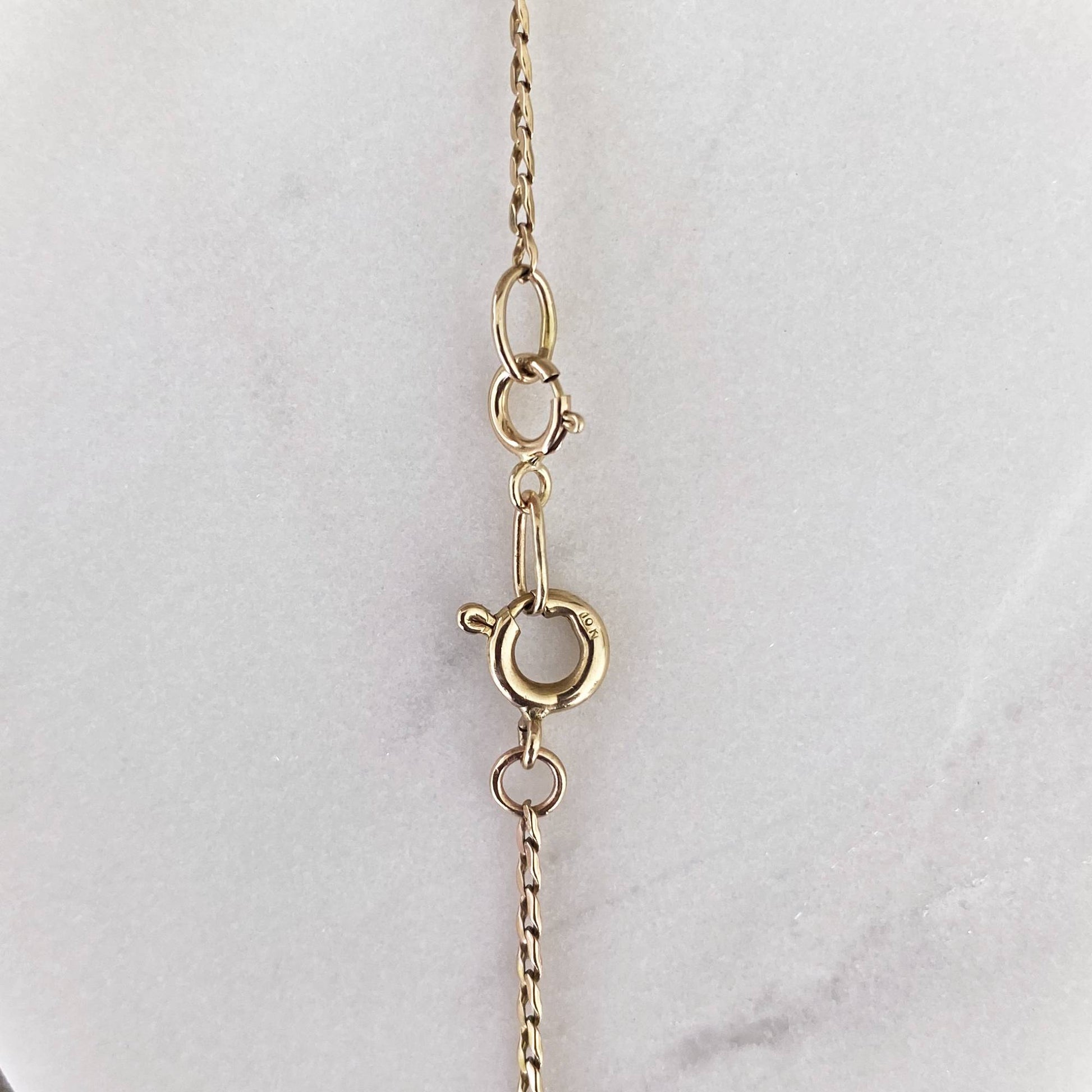 14k gold charm holder clipped onto dainty gold chain on marble display