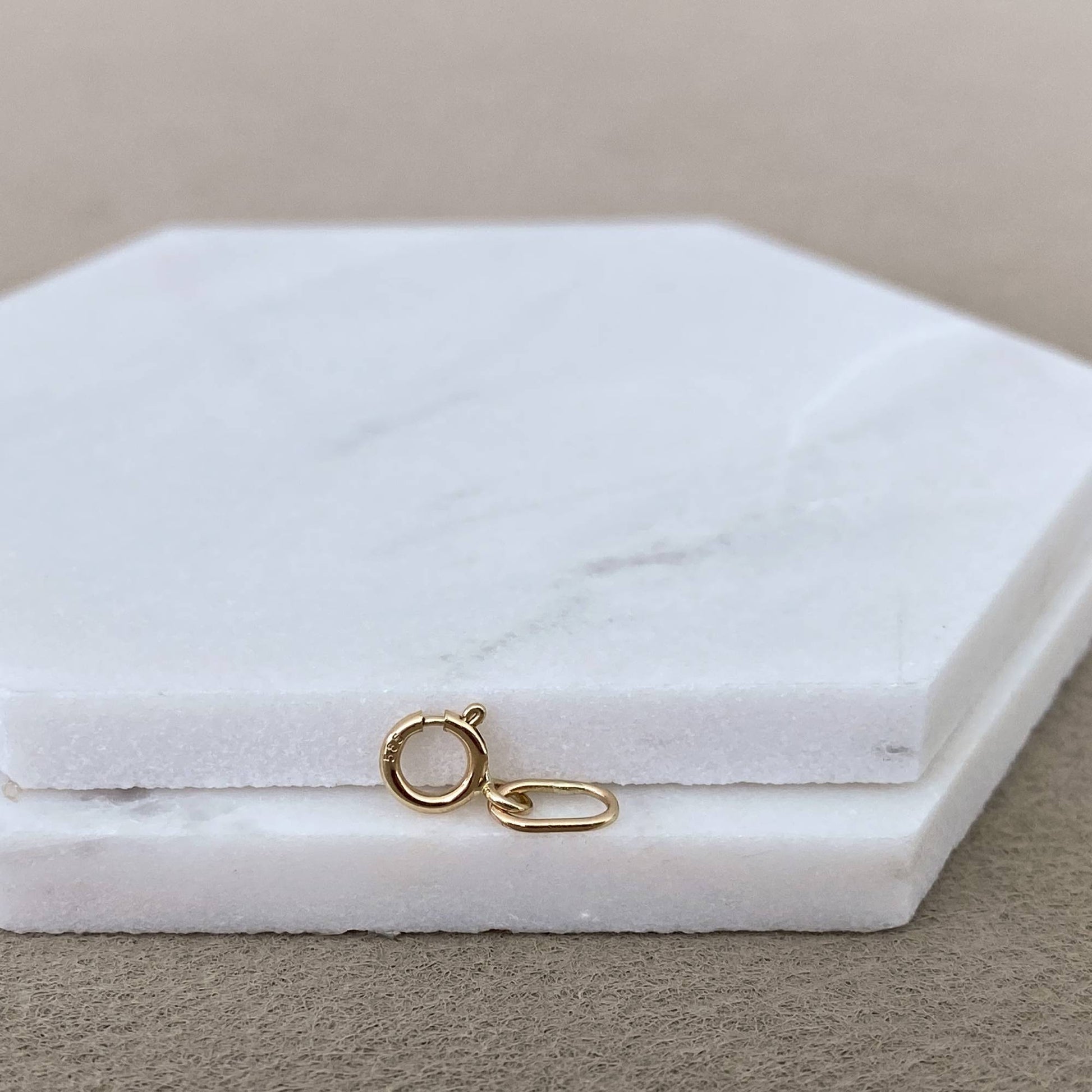 Close-up of handmade 14k solid gold spring ring charm holder on marble