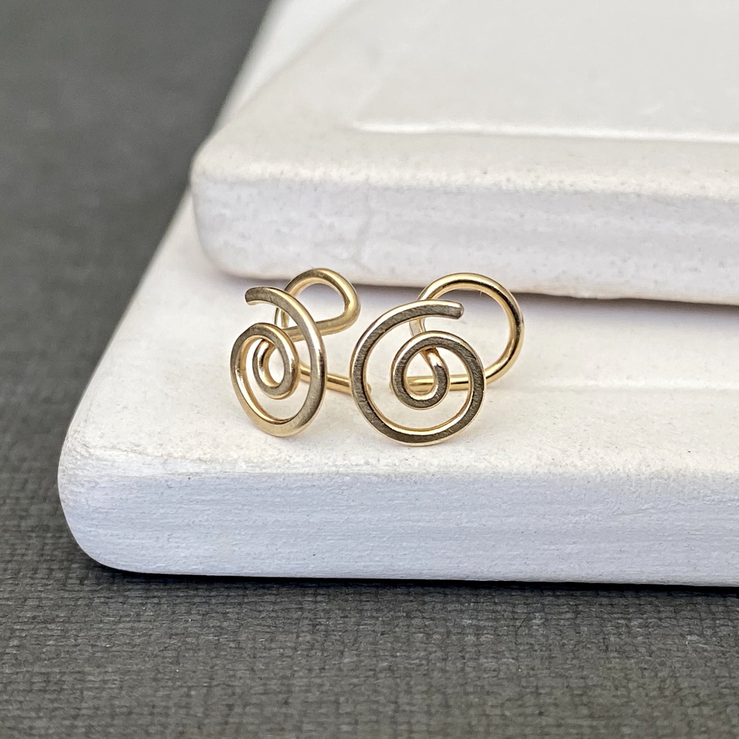 Gold spiral earrings on a white jewelry box with a gray background