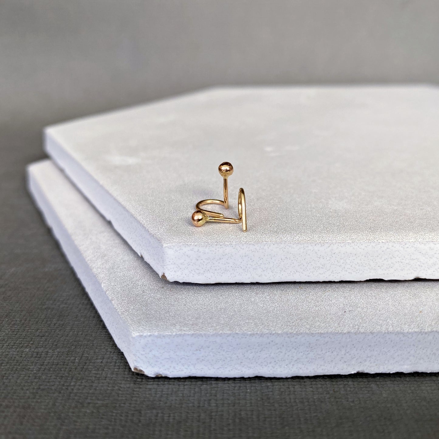 Gold earring ball end stud on a stack of white stones with a gray background