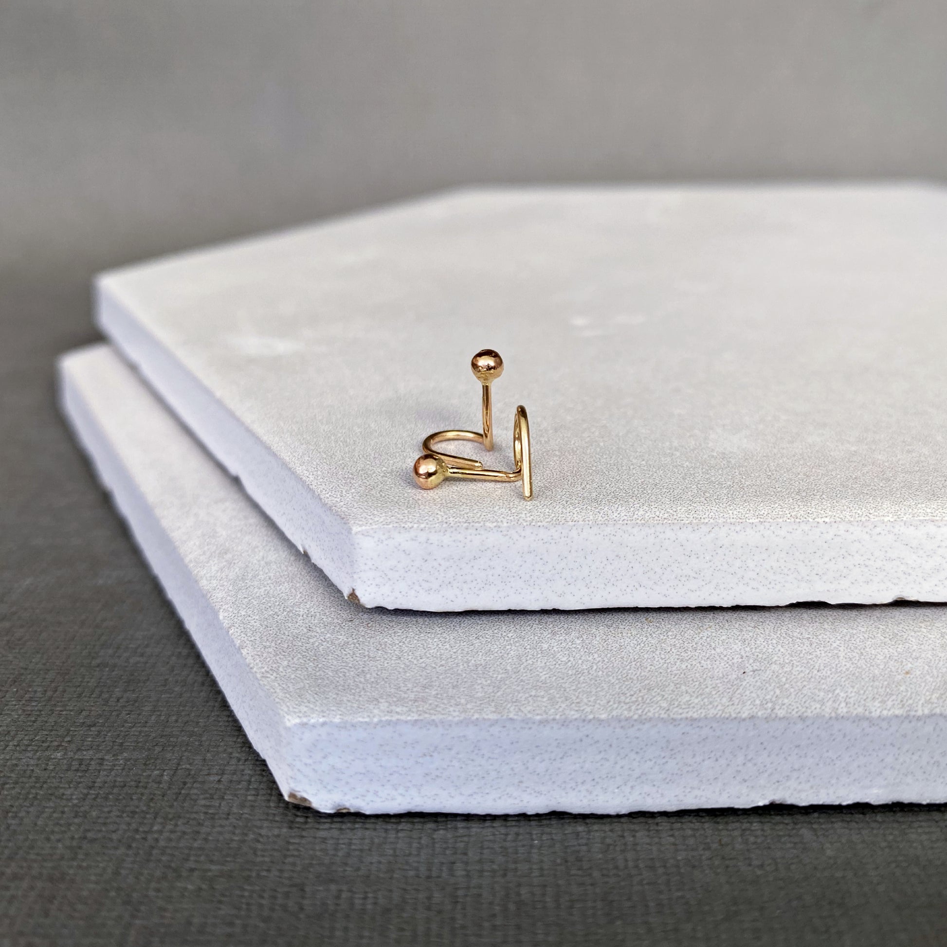 Gold earring ball end stud on a stack of white stones with a gray background