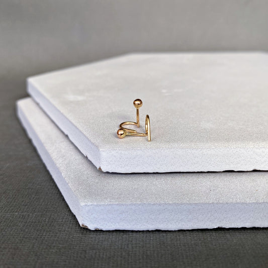 Gold earring ball end stud on a stack of white stones with a gray background