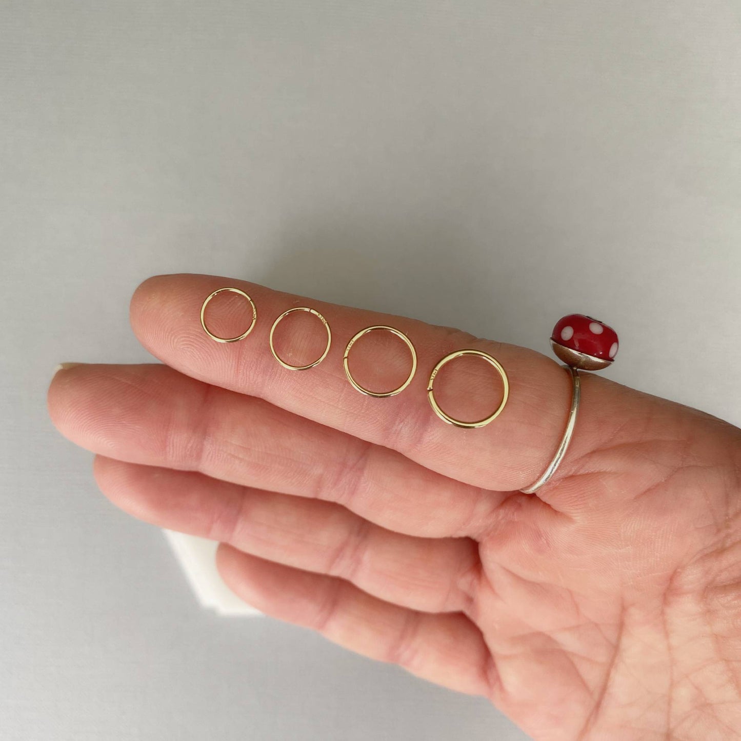 Hand holding four gold rings with a plain background