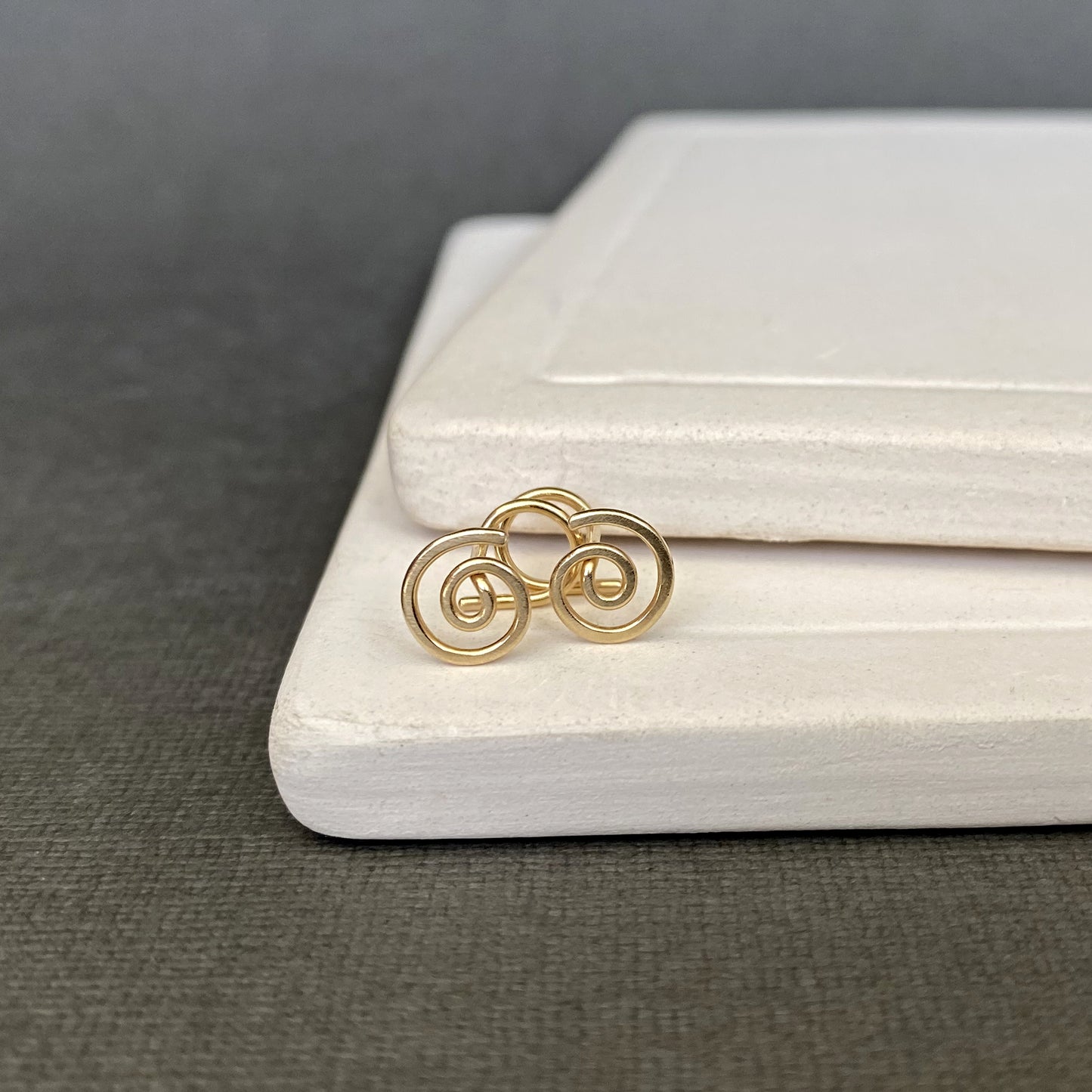 Gold earrings on a white jewelry box with a gray background