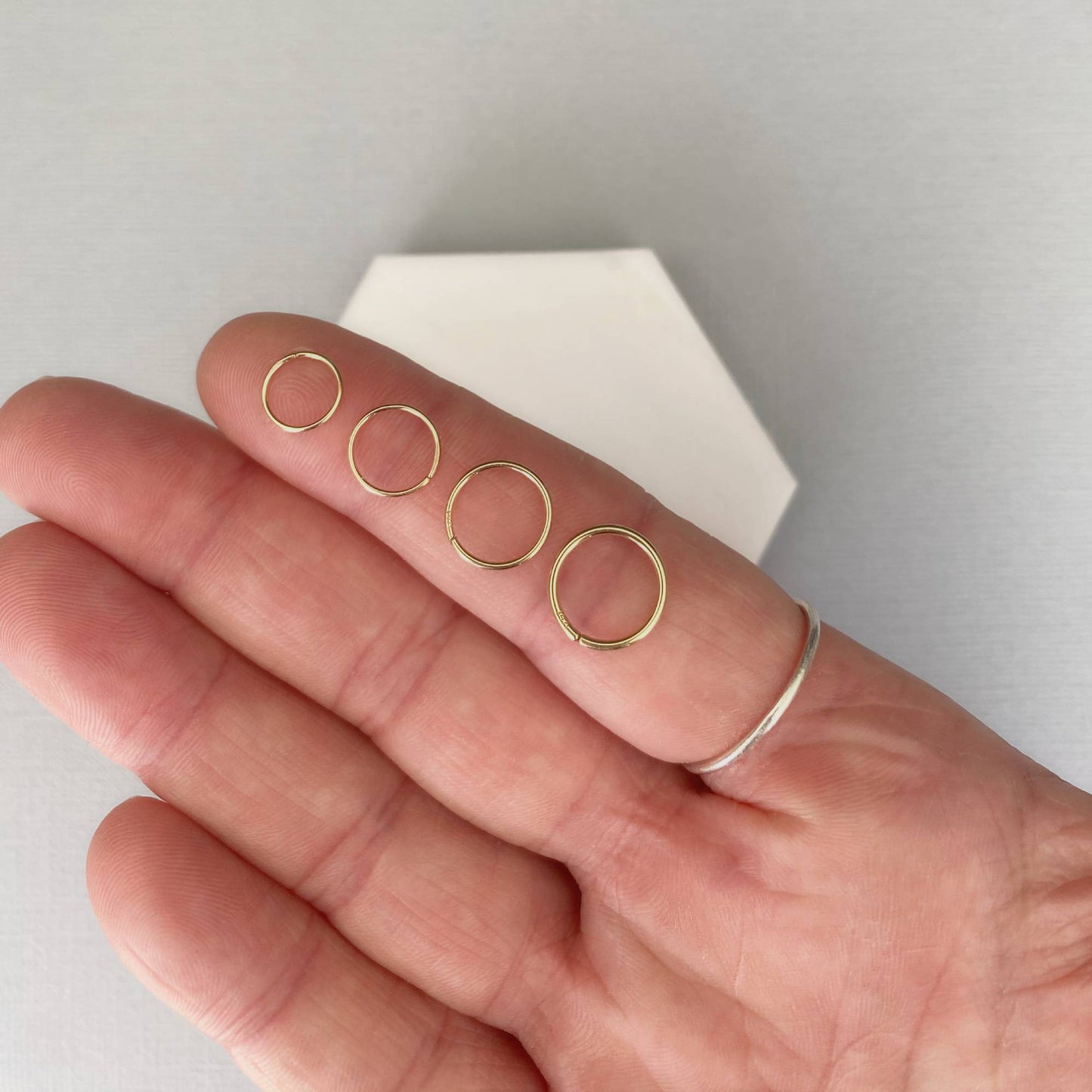 Gold nose rings on a hand with a neutral background