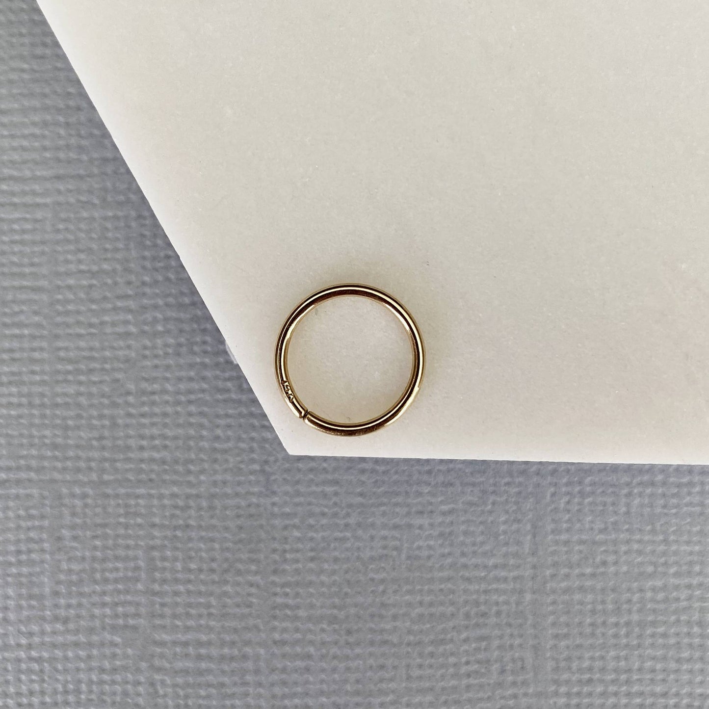 Close up of Gold nose hoop ring on a white card with a gray background