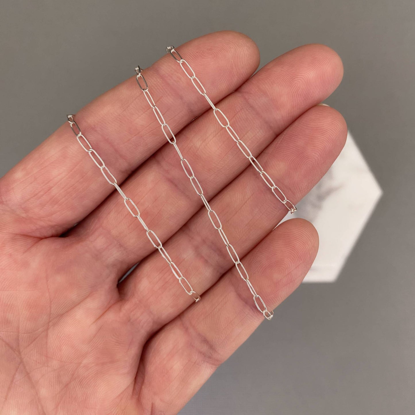 Silver chain held between fingers against a neutral background