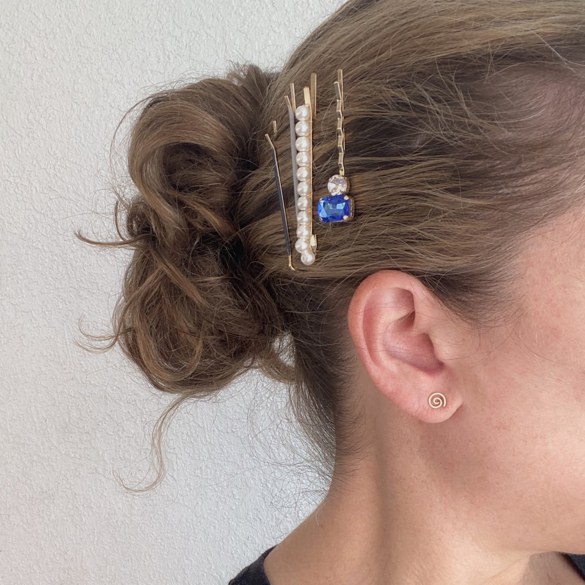 Close-up of a hair bun with decorative hair pins and earrings against a plain background