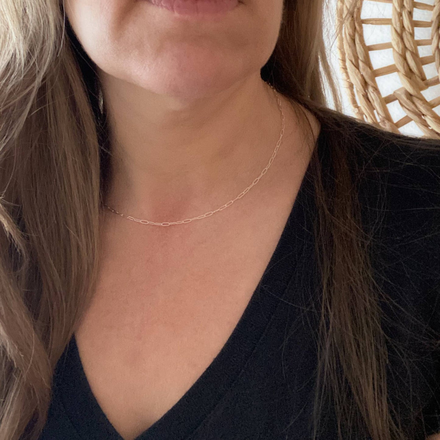 Close-up of a person wearing a delicate sterling silver paperclip necklace with a blurred background