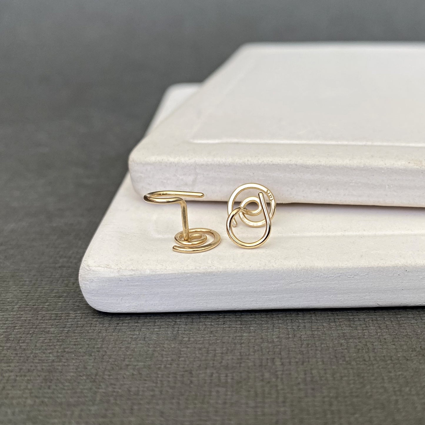 Gold spiral earrings on a gray surface with a white jewelry box.