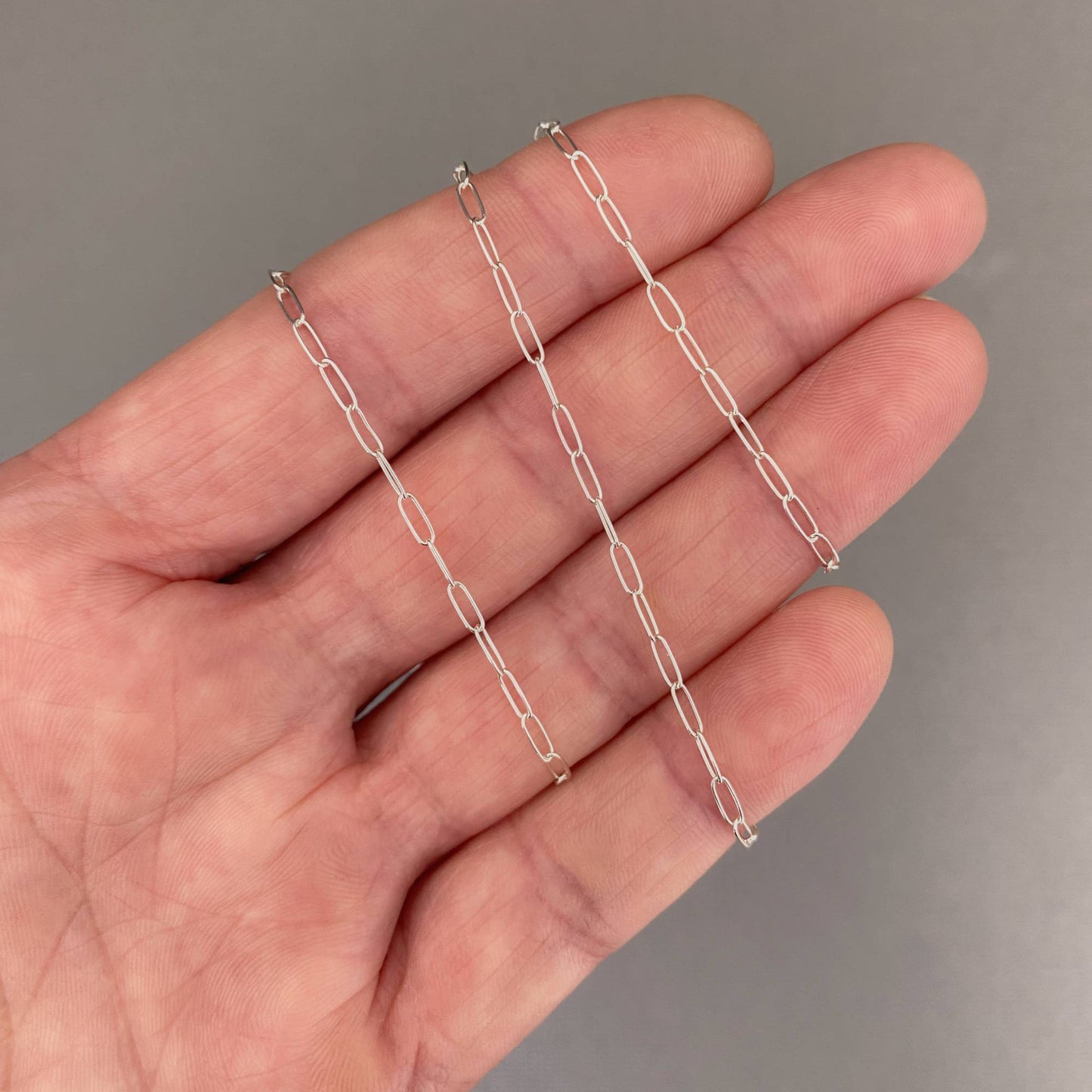 Silver chain held in a hand against a gray background
