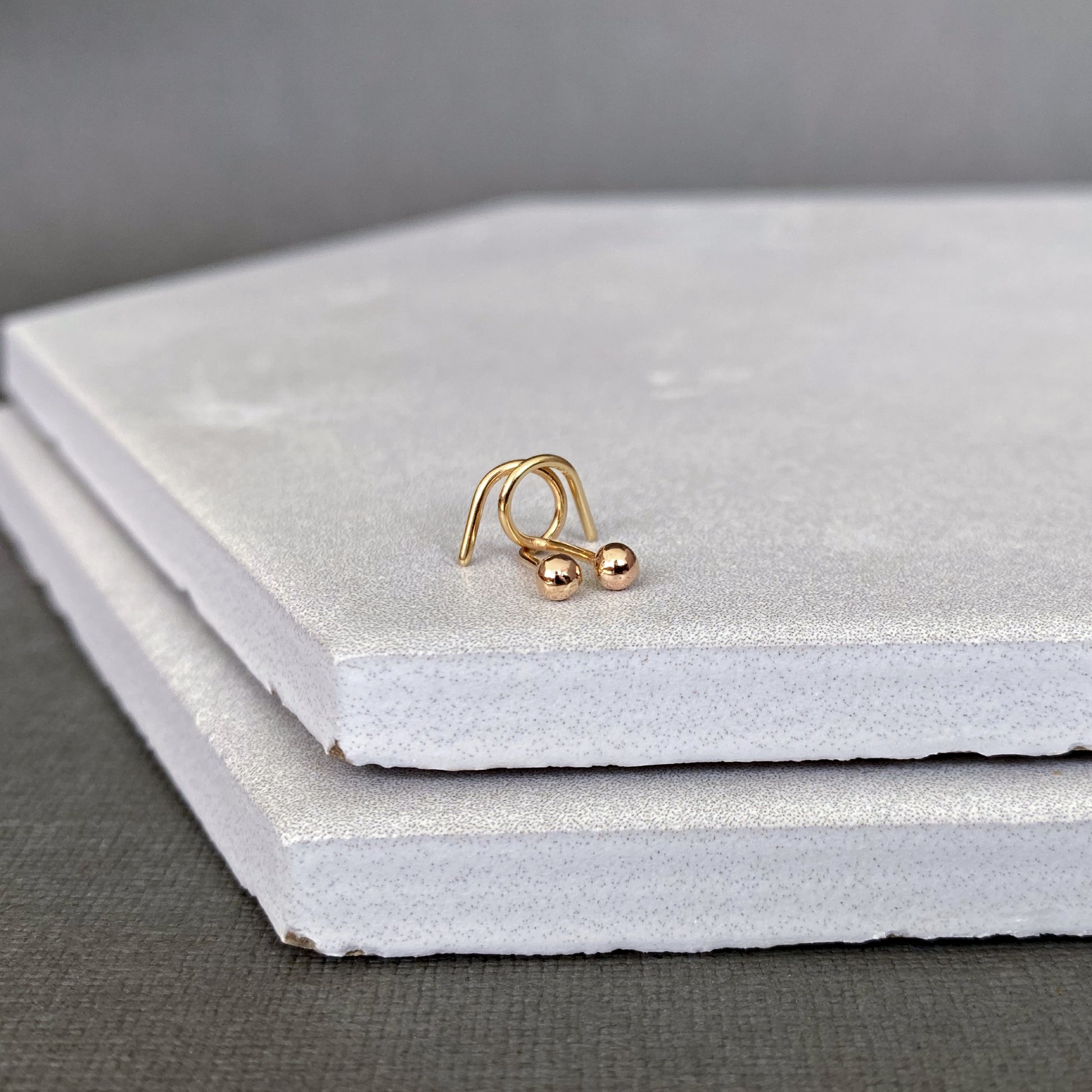 Gold ball end earring stud on a gray surface