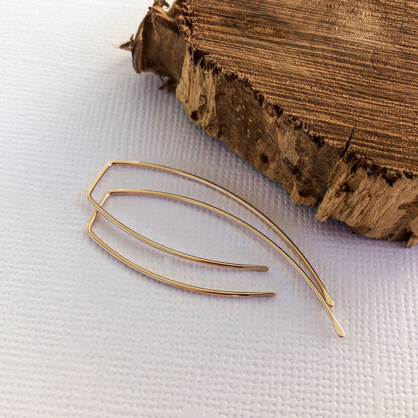 gold filled threader earrings laying next to a wooden block.  You can wear them as is or wrap beads around them.
